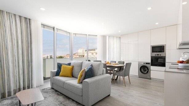 Un apartamento moderno con un sofá gris, una mesa de comedor y una zona de cocina.