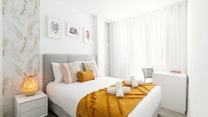 Een moderne slaapkamer met een groot bed, een nachtkastje met een lamp en een raam met dunne gordijnen.