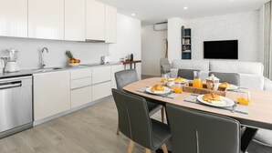 Een moderne keuken met witte kasten, een inbouwvaatwasser en een eethoek met een houten tafel gedekt voor het ontbijt.