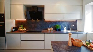 Een moderne keuken met een donker aanrecht, inbouwmeubels, een roestvrijstalen spoelbak en een flatscreen televisie boven het aanrecht.