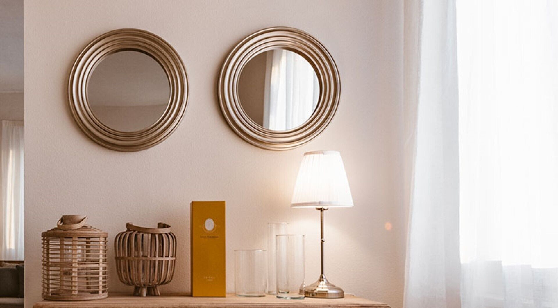 Een kamer met twee spiegels aan de muur, een houten bijzettafeltje met een lamp, een mand en een klein doosje.