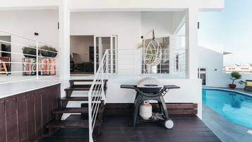 A poolside area with a grill, seating, and a staircase leading to an upper level.