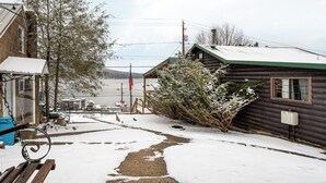 Una cabaña de madera con un patio cubierto de nieve, un cobertizo pequeño y una banca.