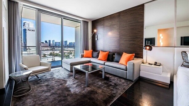 A modern living room with a sofa set, a coffee table, and a view of a cityscape through large windows.