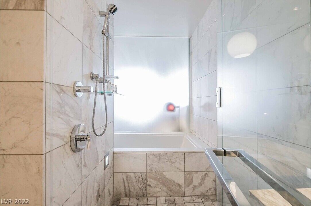 A modern bathroom with a glass-enclosed shower, marble tiles, and a visible window.