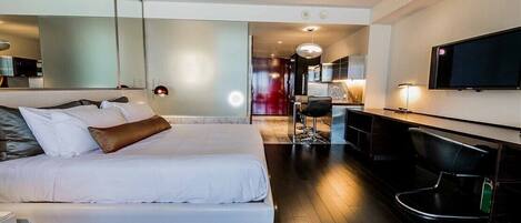 A modern hotel room with a large bed, a desk, a chair, a TV, and a mirror.
