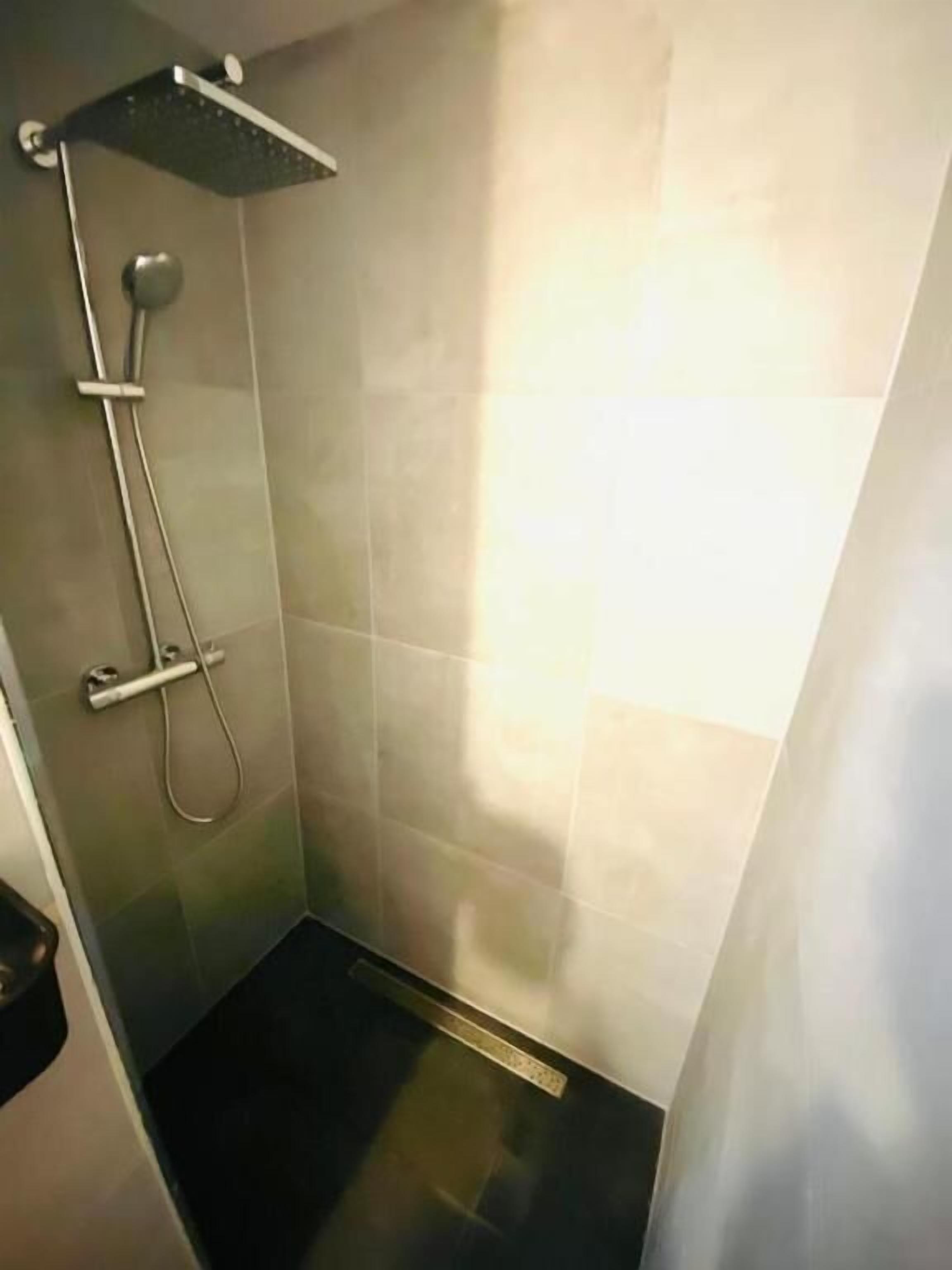 A small, modern shower area with a handheld showerhead and a fixed showerhead.