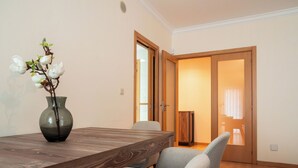 Un comedor con una mesa y sillas de madera, un florero con flores y una puerta que da a otra habitación.