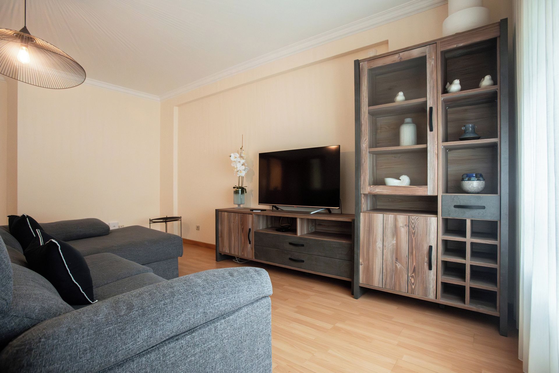 Un salon moderne avec un canapé gris, un téléviseur à écran plat et un meuble en bois doté d’étagères.