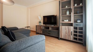 A modern living room with a grey sofa, a flat-screen TV, and a wooden cabinet with shelves.