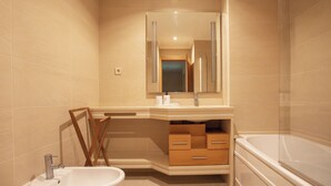 A modern bathroom with a large mirror, a sink, a vanity with drawers, and a bathtub.