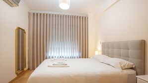 Una habitación de hotel con una cama grande, una mesita de noche, un espejo y una ventana con cortinas.