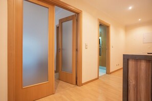 Un pasillo con puertas de madera, suelo de madera y una cocina visible a través de una puerta abierta.