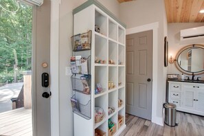 A well-organized entryway with a white shelving unit, a doorbell, a trash can, and a mirror.