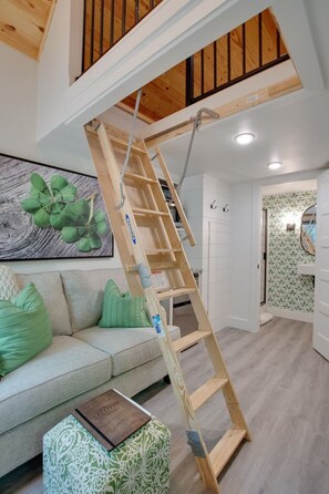 A loft-style room with a wooden ladder, a sofa, and a patterned ottoman.