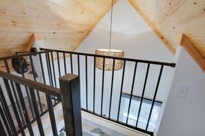 Eine Holzbalkendecke mit geneigter Form, einem schwarzen Metallgeländer und einer hängenden Leuchte.
