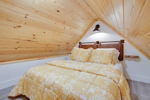 A bedroom with a wooden sloped ceiling, a bed with floral bedding, and a nightlight above the bed.