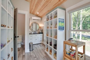 A bathroom with a wooden ceiling, white cabinetry, a round mirror, and a window with a view of trees.