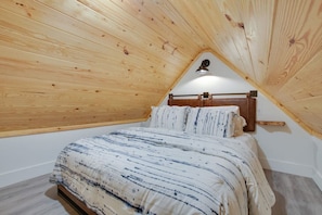 A small, cozy bedroom with a sloped ceiling and wooden paneling.