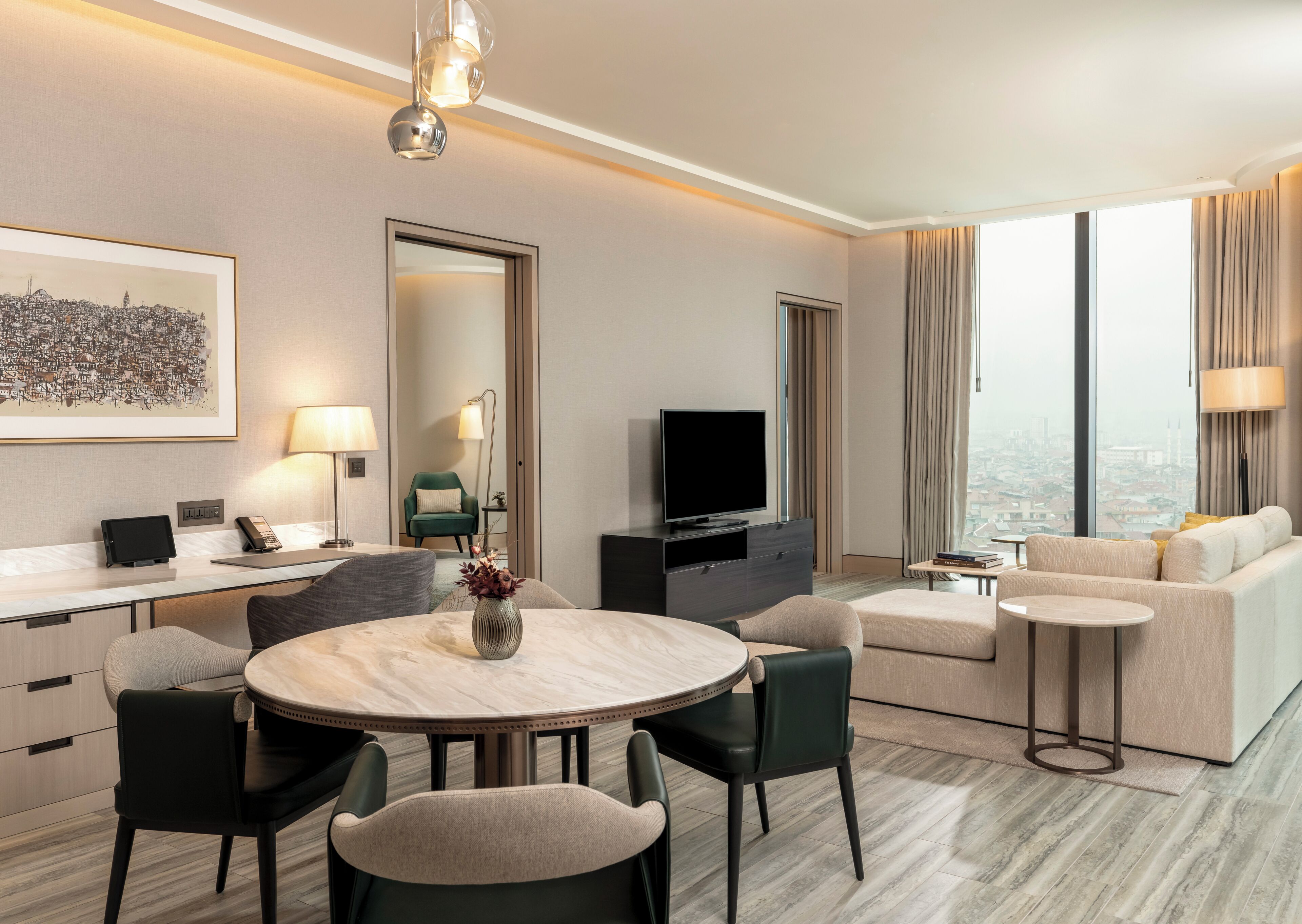A modern hotel room with a dining area, a sofa set, a TV, and a city view.