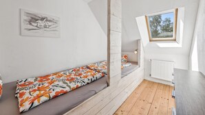 Una camera da letto in stile loft con pavimento in legno, un letto con lenzuola a motivi floreali, un lucernario, un termosifone e un quadro appeso al muro.
