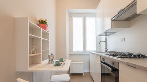 Een compacte keuken met witte kasten, een gasfornuis en een raam dat voor natuurlijk licht zorgt.