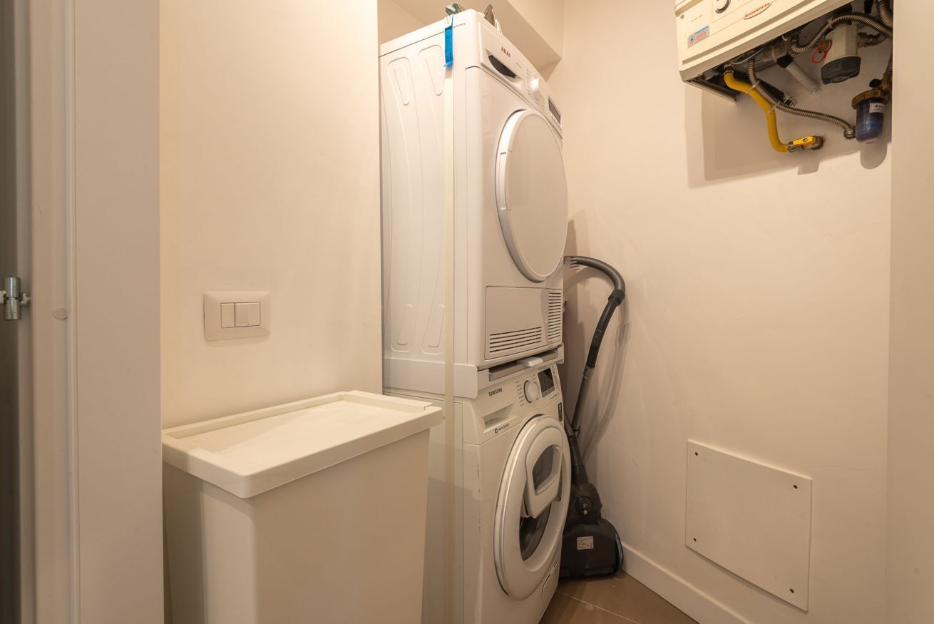 A compact laundry room with a stacked washer and dryer, a small sink, and a vacuum cleaner.