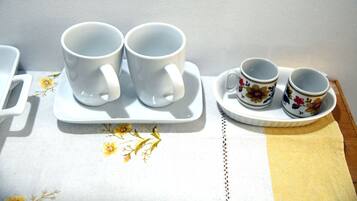 Uma mesa com dois copos brancos sobre um guardanapo floral, uma bandeja branca com duas xícaras florais e uma alça branca à esquerda.