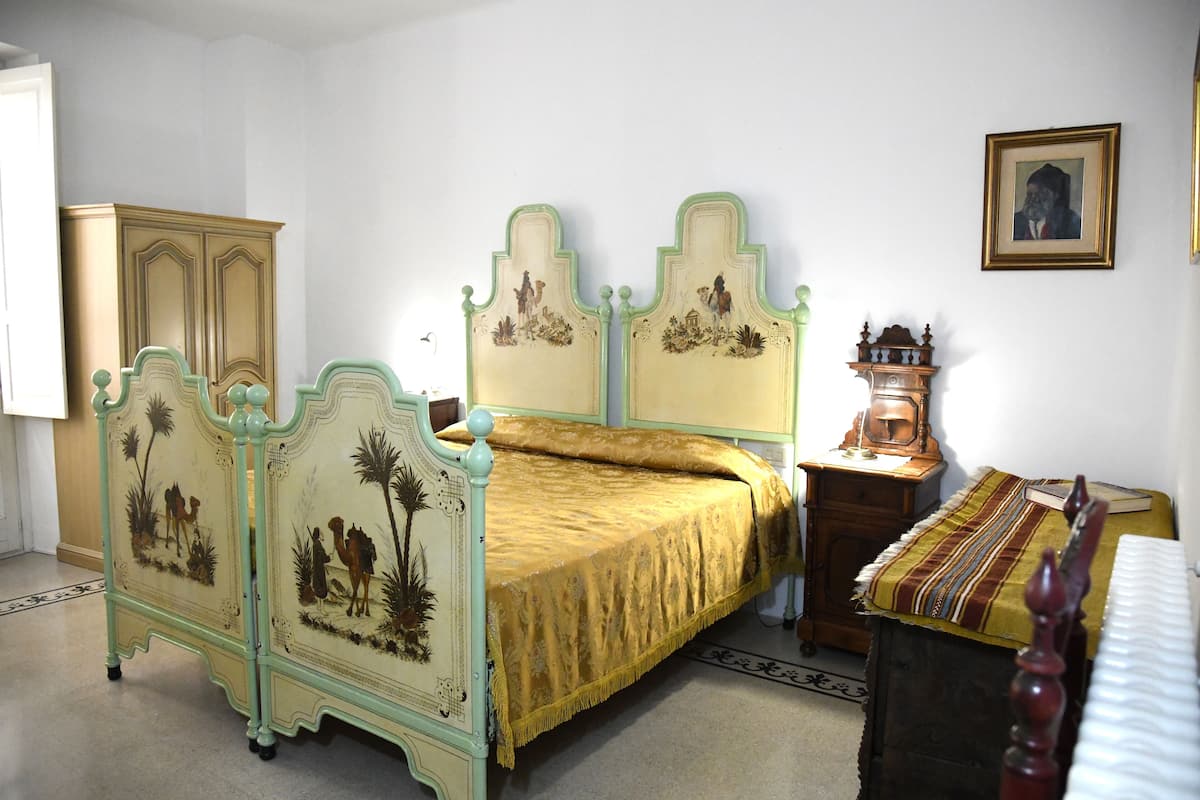 A room with a bed, a wooden cabinet, a small table with a lamp, and a framed picture on the wall.