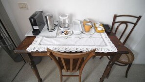 A wooden dining table with a white lace tablecloth, a coffee maker, cups, and a remote control. - Domo Peonia Bianca (Nuoro)