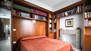 A room with a bed, wooden bookshelves, a fireplace, and a framed picture on the wall. - Domo Peonia Bianca (Nuoro)