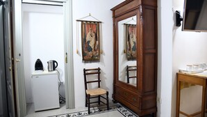 A compact room with a white refrigerator, a wooden chair, a large mirror, and a small table with a kettle and cups. - Domo Peonia Bianca (Nuoro)