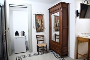 Habitación compacta con refrigerador blanco, una silla de madera, un espejo grande y una mesita con tetera y tazas.