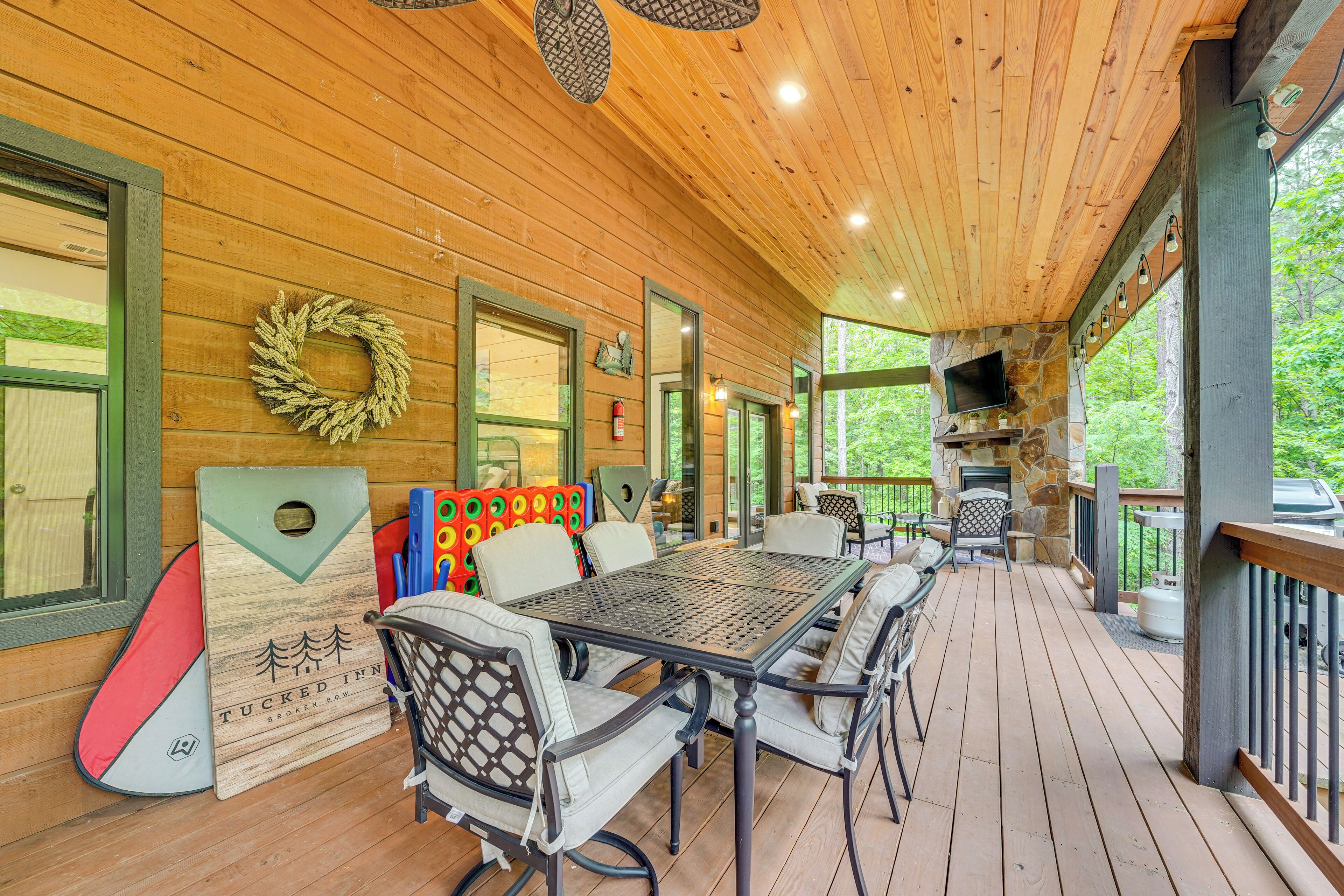 A wooden deck with a table and chairs, a stone fireplace, and a television.