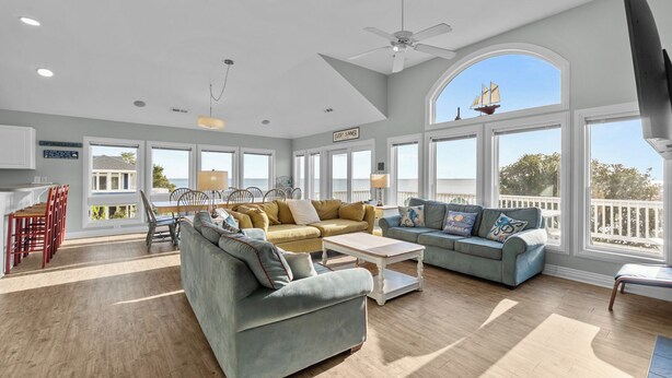A spacious living room with large windows, a ceiling fan, and a view of the ocean. - 1528 - Sound and Color - Spacious Soundfront Retreat w/ Stunning Sunsets (Corolla)