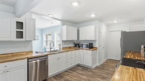 A modern kitchen with white cabinetry, a stainless steel dishwasher, a microwave, and a refrigerator.