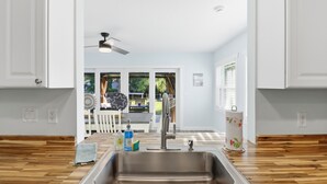 A kitchen with a stainless steel sink, wooden flooring, and white walls.