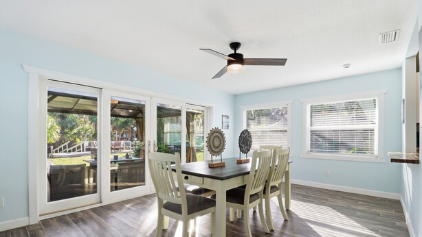 A dining area with a table and chairs, a ceiling fan, and large windows.