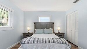 A bedroom with a bed, two bedside tables with lamps, a window with blinds, and a wardrobe.