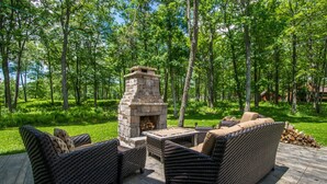 An outdoor patio with wicker furniture and a stone fireplace surrounded by a forest. - Biltmore Chalet by Taylor Made Deep Creek (McHenry)
