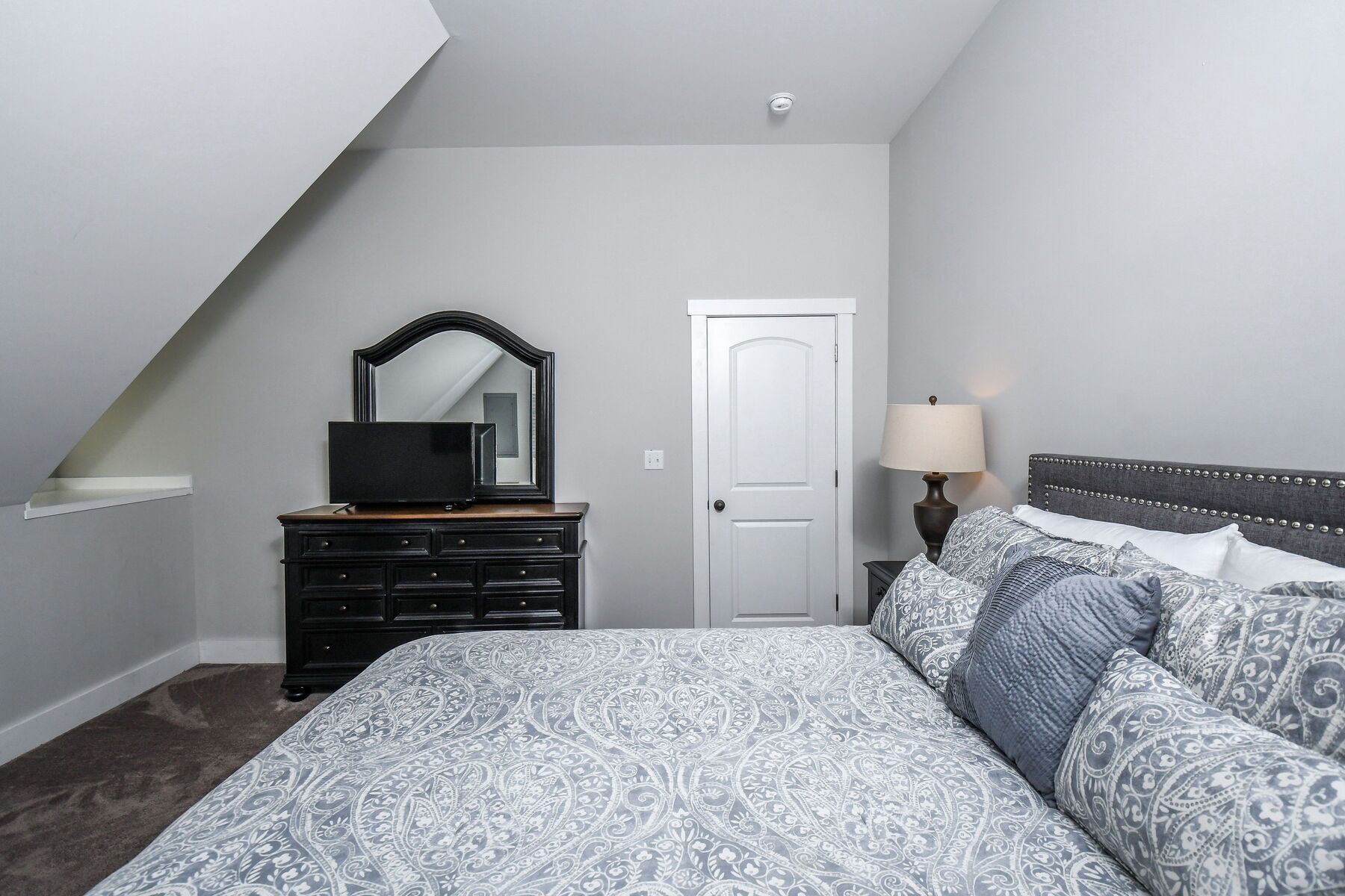 A bedroom with a bed, dresser, mirror, door, and nightstand.