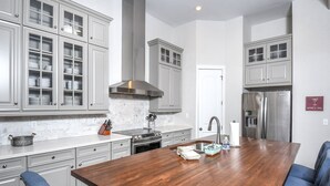 A modern kitchen with grey cabinets, a stainless steel refrigerator, and a wooden dining table with blue chairs. - Biltmore Chalet by Taylor Made Deep Creek (McHenry)