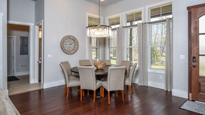 A dining area with a round table, six chairs, a chandelier, and large windows with blinds. - Biltmore Chalet by Taylor Made Deep Creek (McHenry)