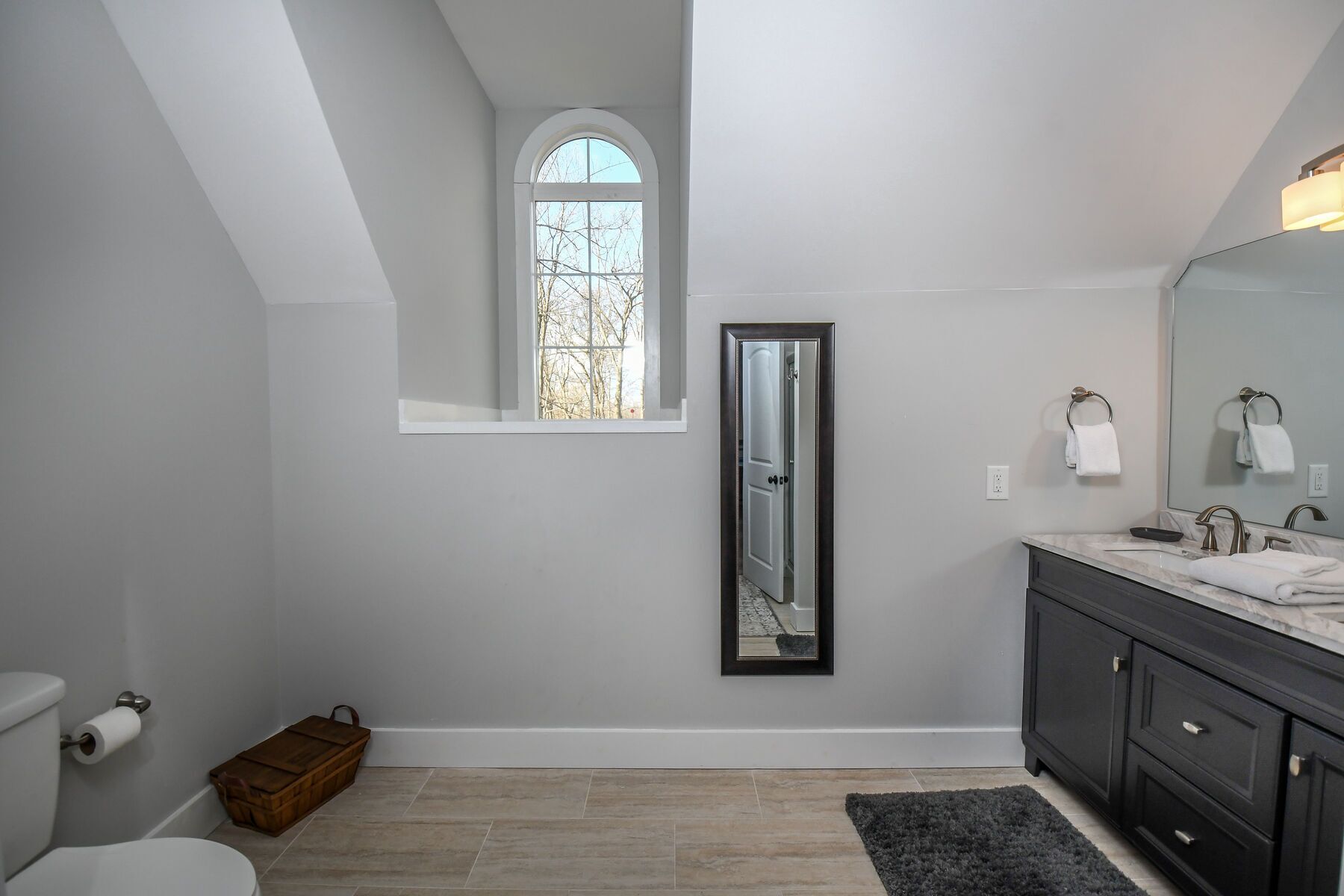A modern bathroom with a skylight, a large mirror, a dark vanity, and a small window.
