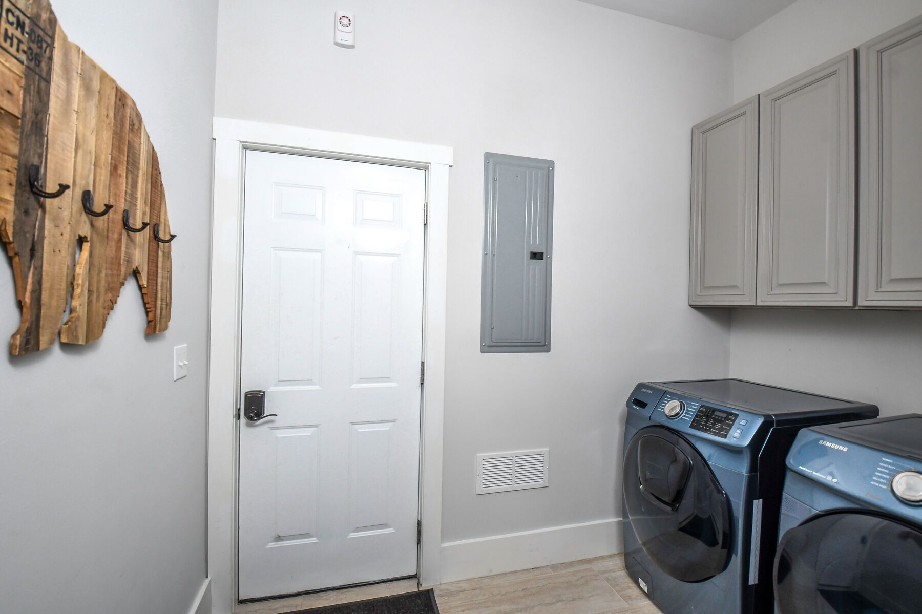 A laundry room with a front-loading washing machine, a white door, and a wooden wall decoration.