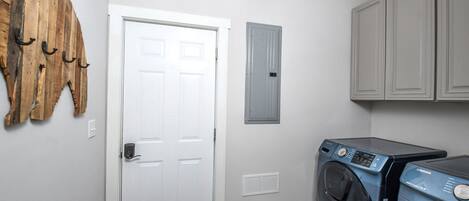 A laundry room with a front-loading washing machine, a white door, and a wooden wall decoration.