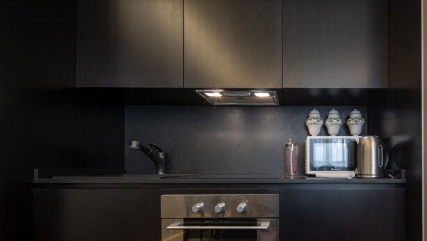 A modern kitchen with dark cabinetry, a built-in oven, a microwave, and a kettle. - Serragli Suite An in Santo Spirito Area (Firenze)