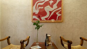 Une table à manger avec deux chaises, un vase contenant une seule rose, une bouteille, un verre et une boîte.