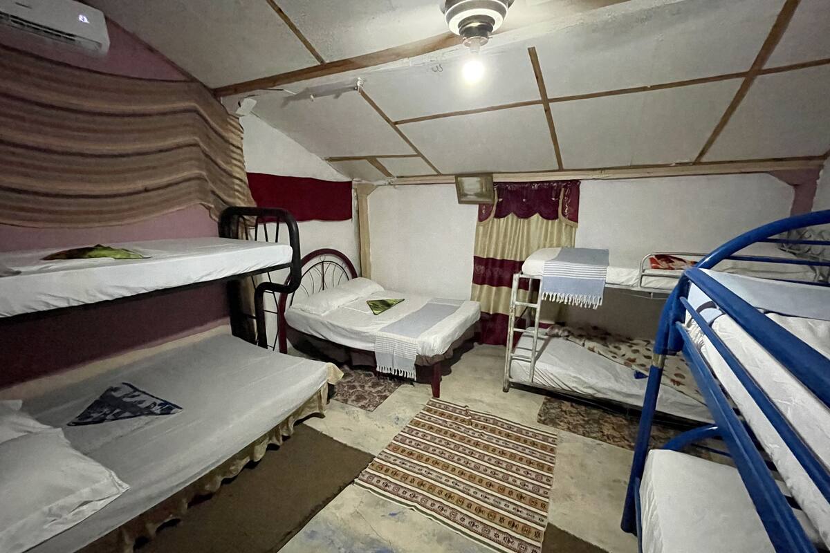 A dormitory room with bunk beds, a ceiling fan, a radiator, and a patterned rug.