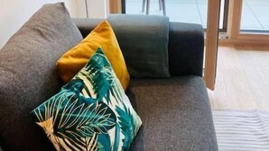 Moderni olohuone, jossa on harmaa sohva, pieni pyöreä pöytä ja liukuovet, jotka johtavat ulos parvekkeelle.